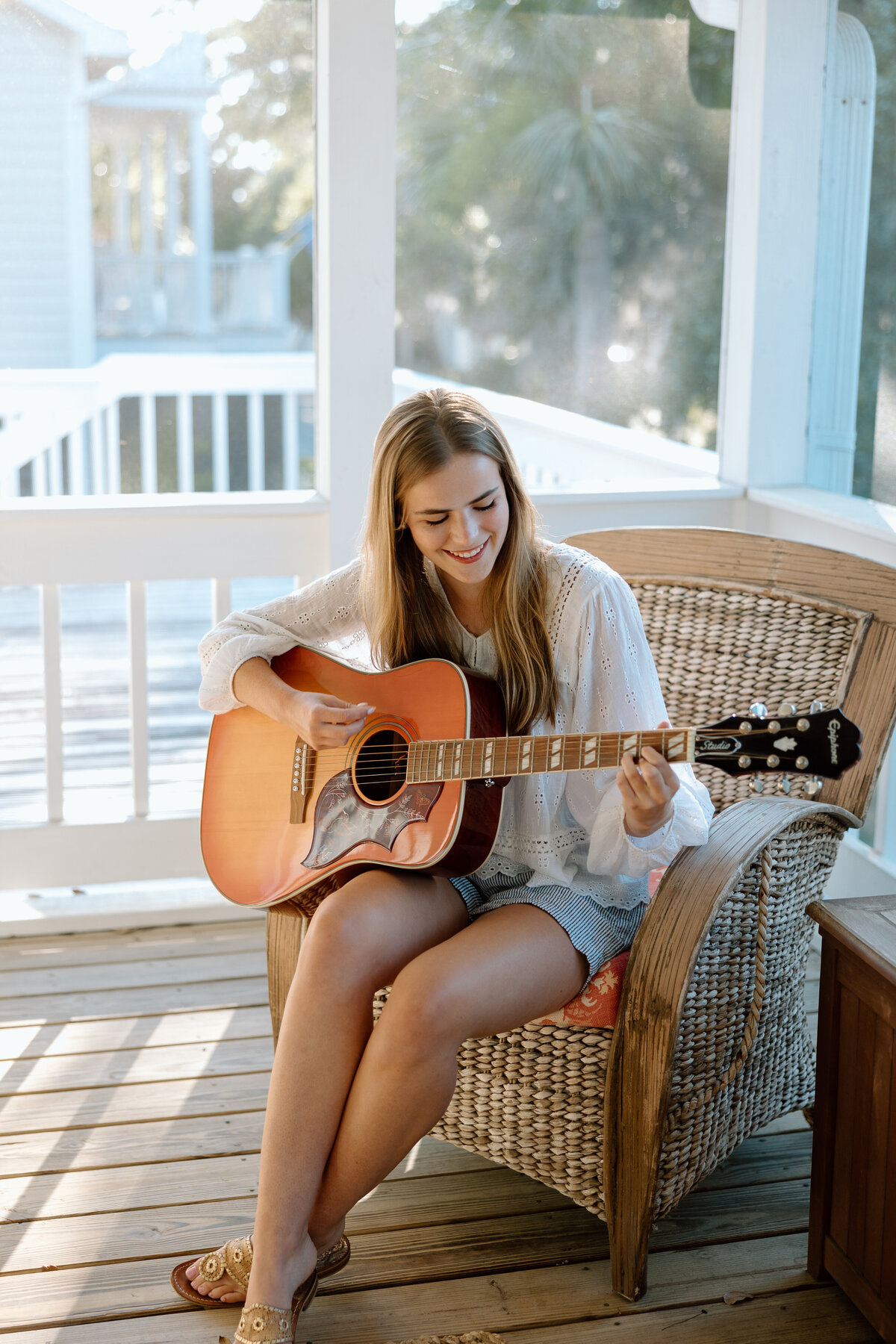 Senior photos at Edisto beach, senior sits on porch with a guitar