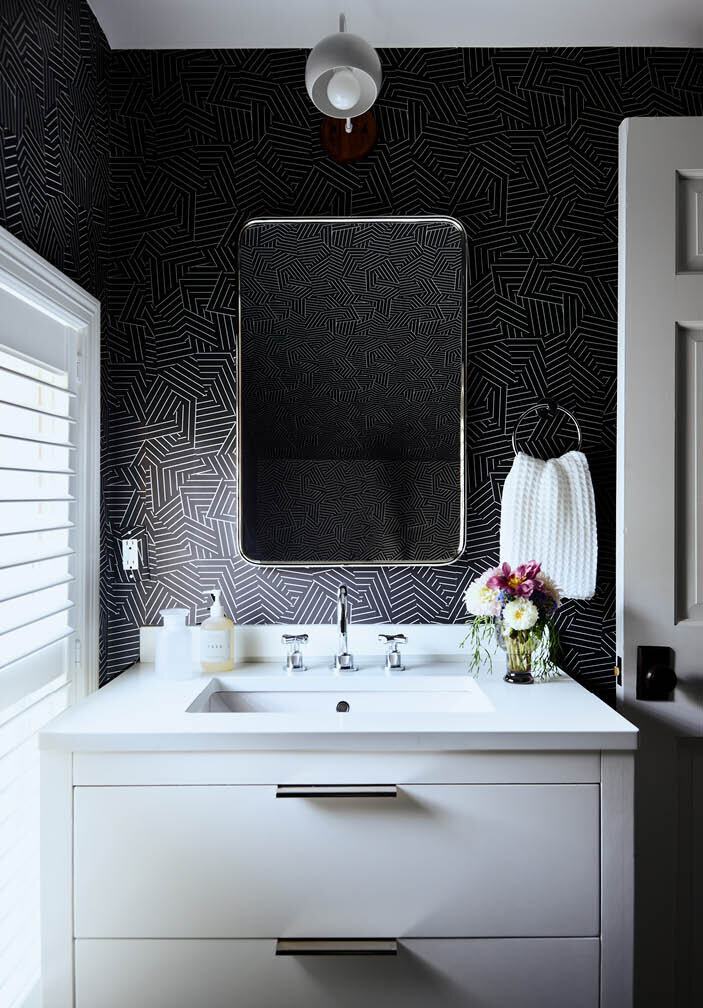 Discover the attic bath in a historic Hingham home, featuring black wall and floor tiles, a walk-in shower, and a contrasting white vanity for a bold, stylish look.