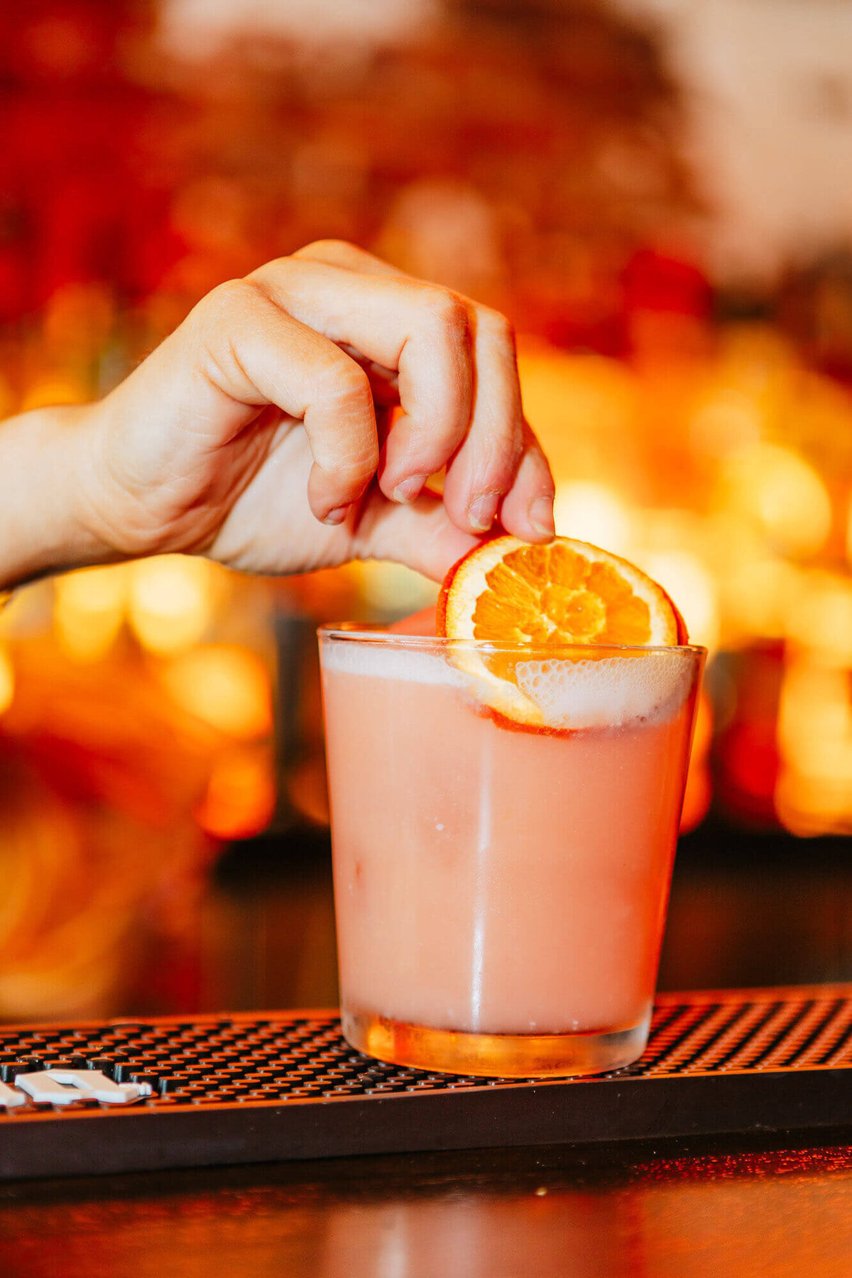 hand adding an orange to garnish a cocktail