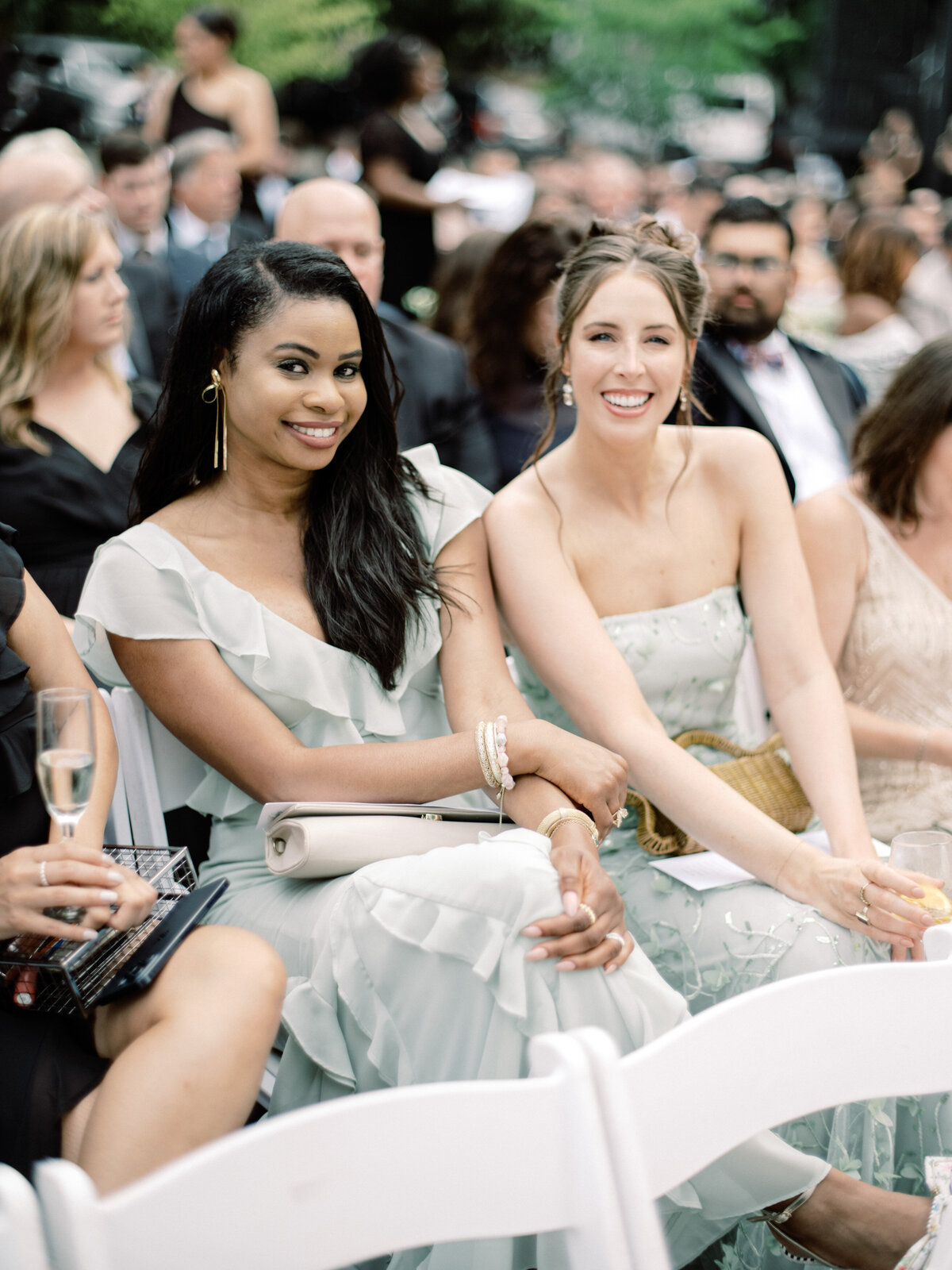 Two fashionable women smiling and posing together at an event, reflecting the joy of companionship and the shared experience of elegance and celebration.