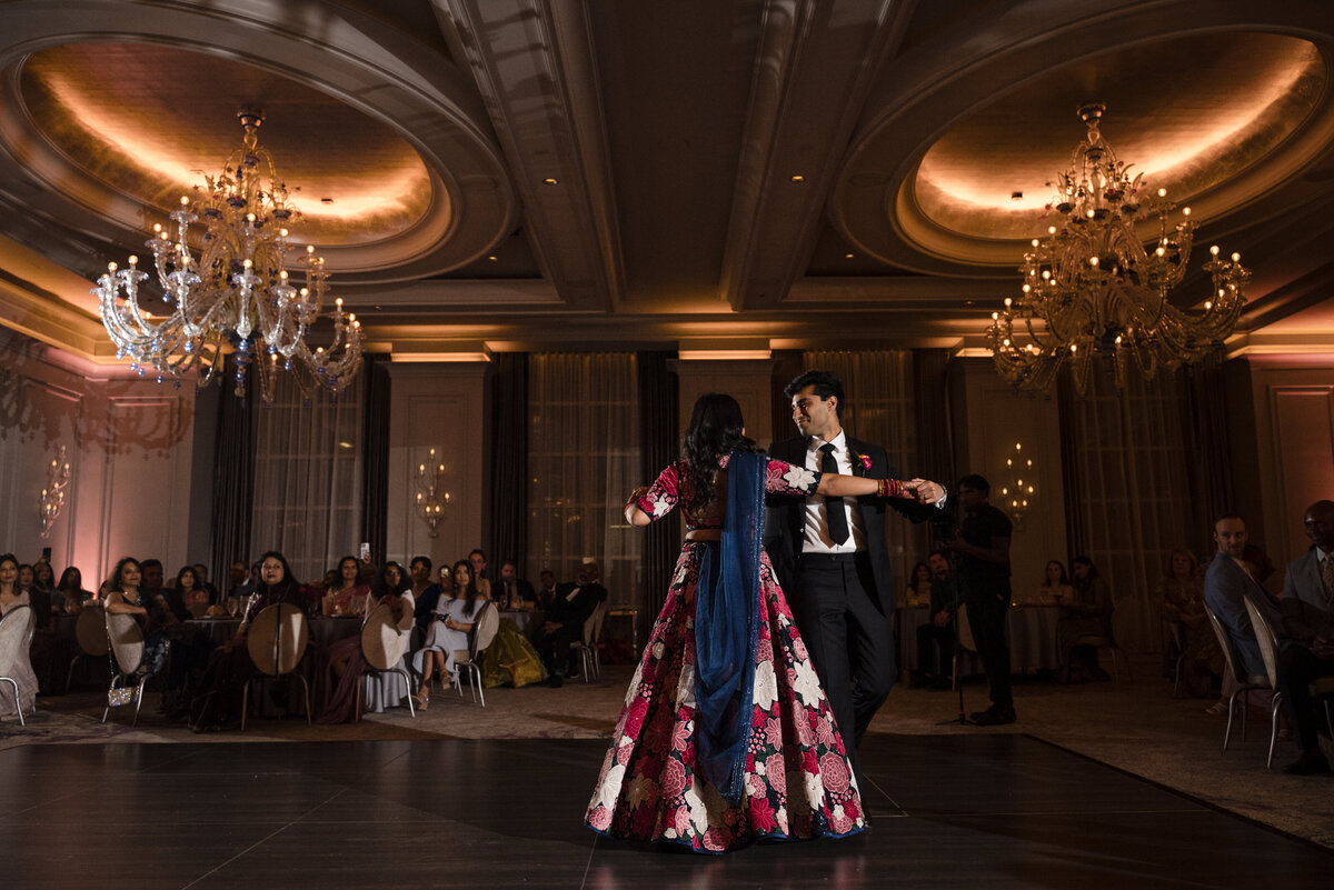 Indian wedding reception photography at the Grand Bohemian Hotel Charlotte. A joyful bride in a vibrant floral lehenga shares a candid dance moment with her groom in a black tuxedo. Captured by a Charlotte Indian wedding photographer specializing in candid, romantic wedding photography.  