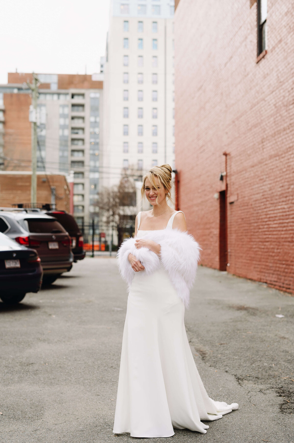 outdoor wedding photo of bride in an alley way in downtown Richmond while she wears a white fur coat over we wedding dress outside the common house richmond wedding venue
