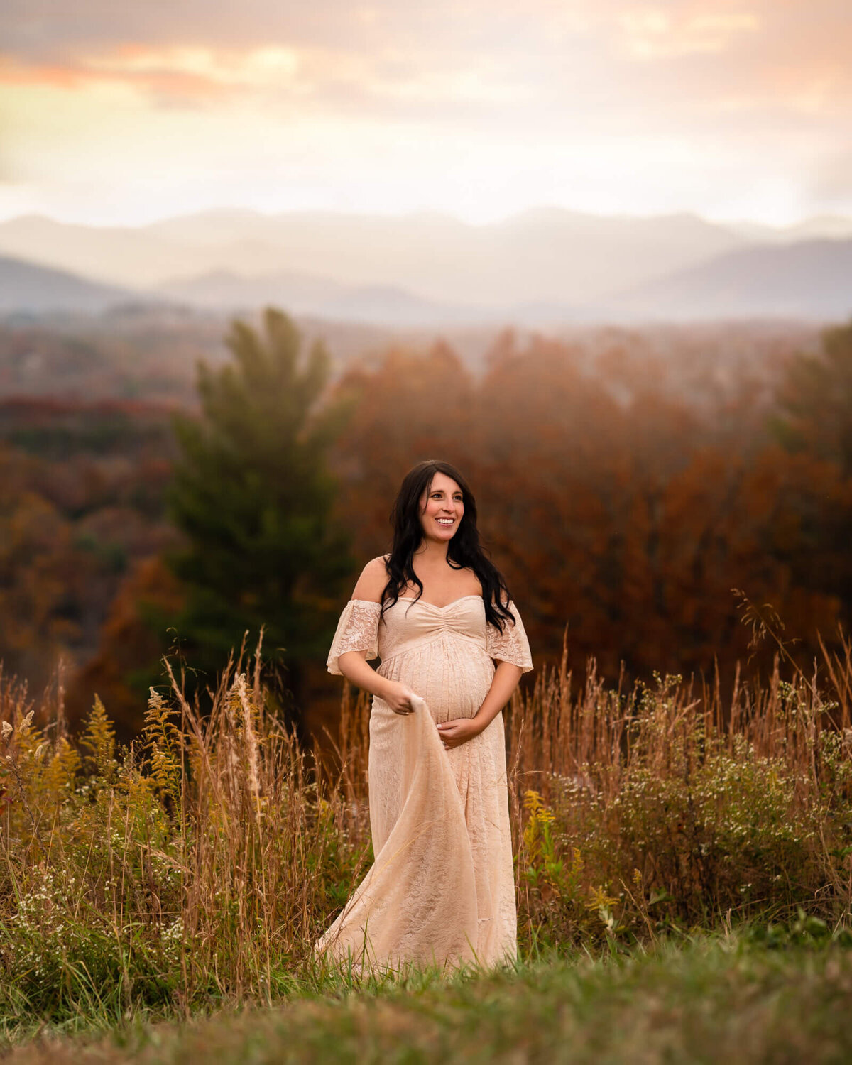 A beautiful pregnant girl in a long lace gown holds her bump and laughs
