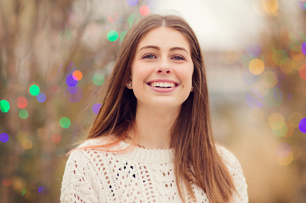 Headshot of a girl with brown hair and pretty smile with Christmas lights.