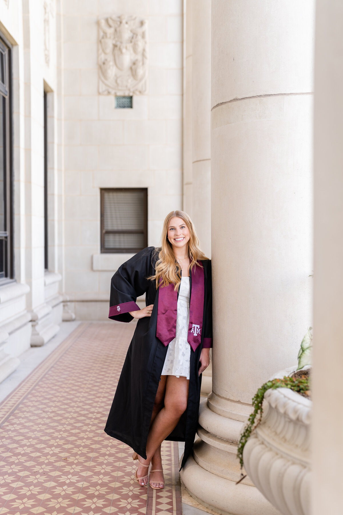 Texas A&M senior girl wearing gown and Aggie stole and leaning on column with hand on hip in columns of Administration Building