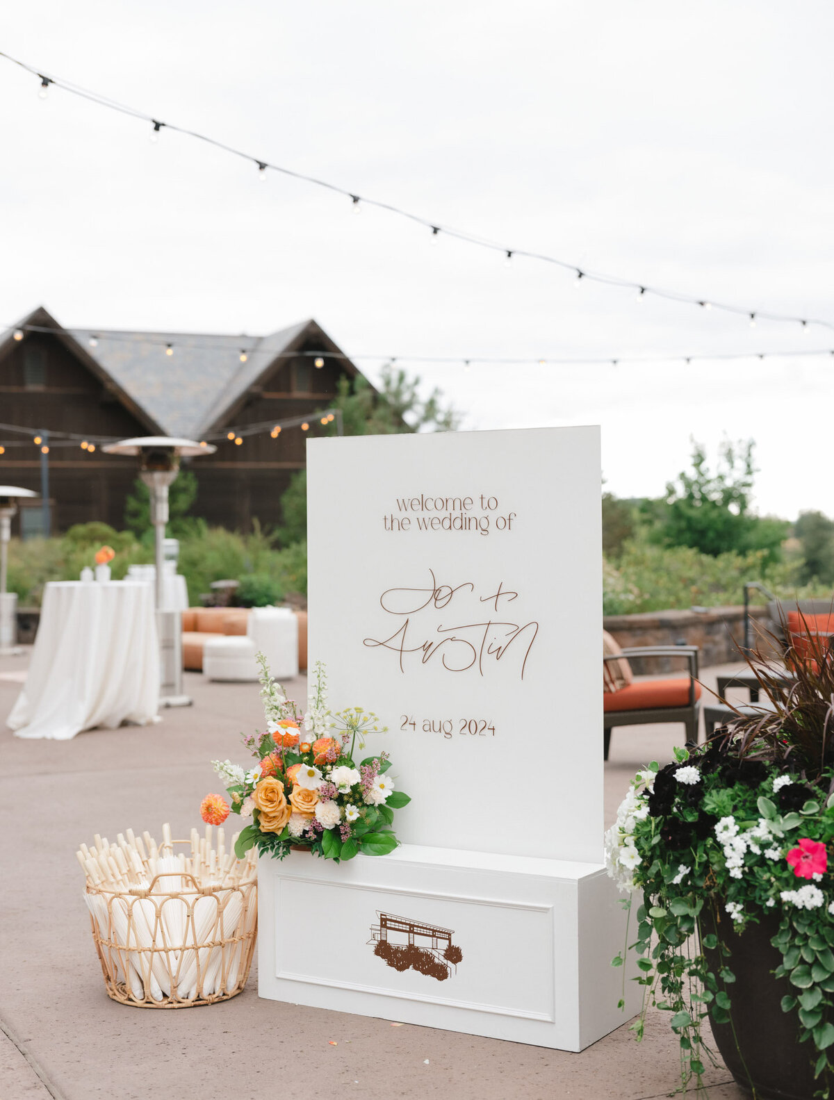 custom calligraphy welcome sign on a luxury wedding venue patio with florals and a basket of umbrellas representing full service design and calligraphy by Life in Letters.