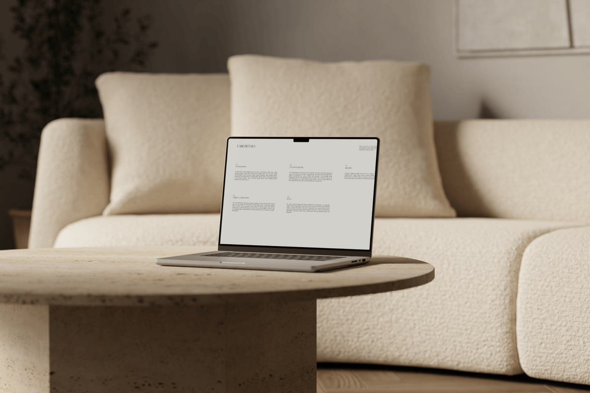 A laptop rests on a travertine coffee table, showcasing a page from the Virtual Interior Styling Handover Guide. The soft textures of a cream bouclé sofa gently blur in the background, creating a refined and stylish setting.