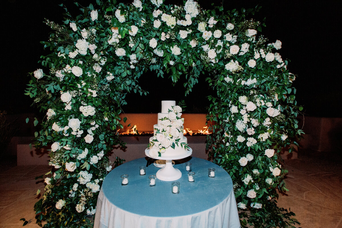 A stunning multi-tiered wedding cake elegantly displayed under a lush floral arch, creating a breathtaking focal point at this luxury wedding.