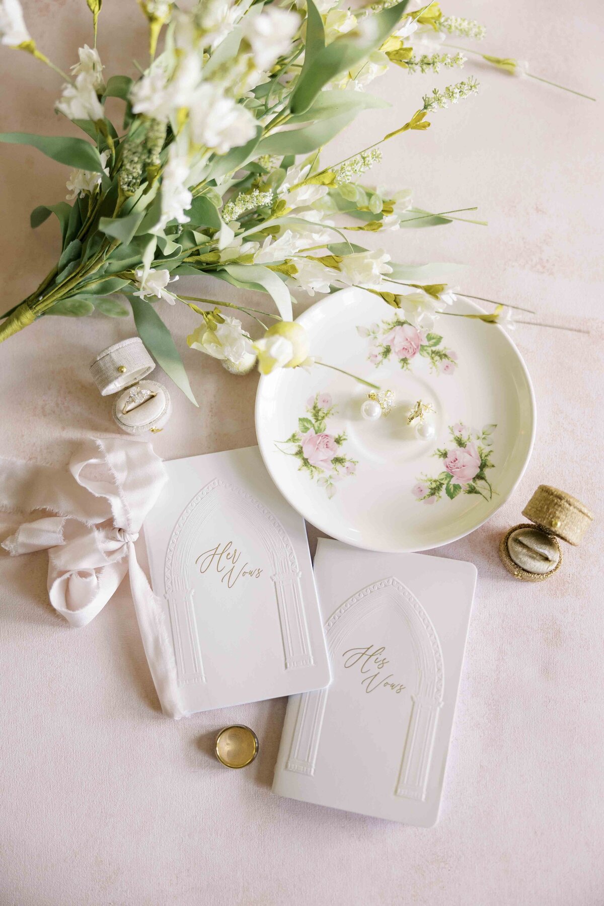 a pink themed wedding flat lay with vow books, flowers, and jewelry