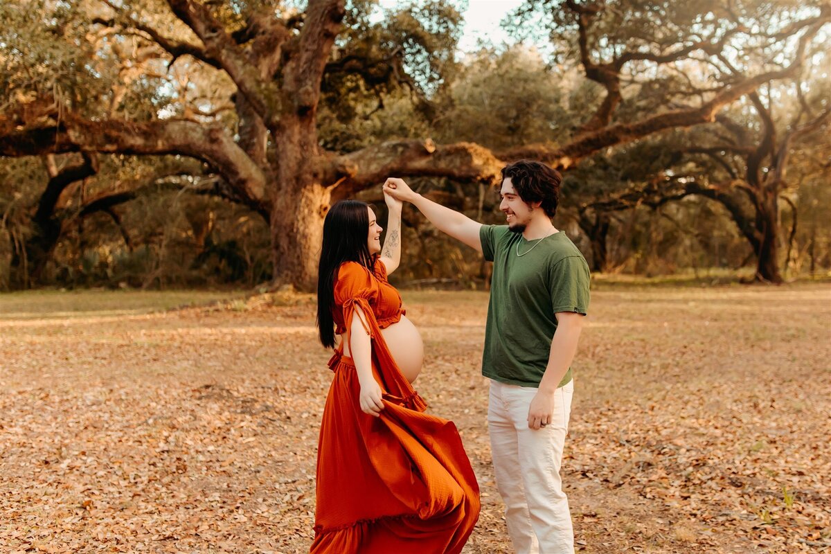 Baytown, Tx an expecting woman dancing in a flowy rust dress with a man smiling photos