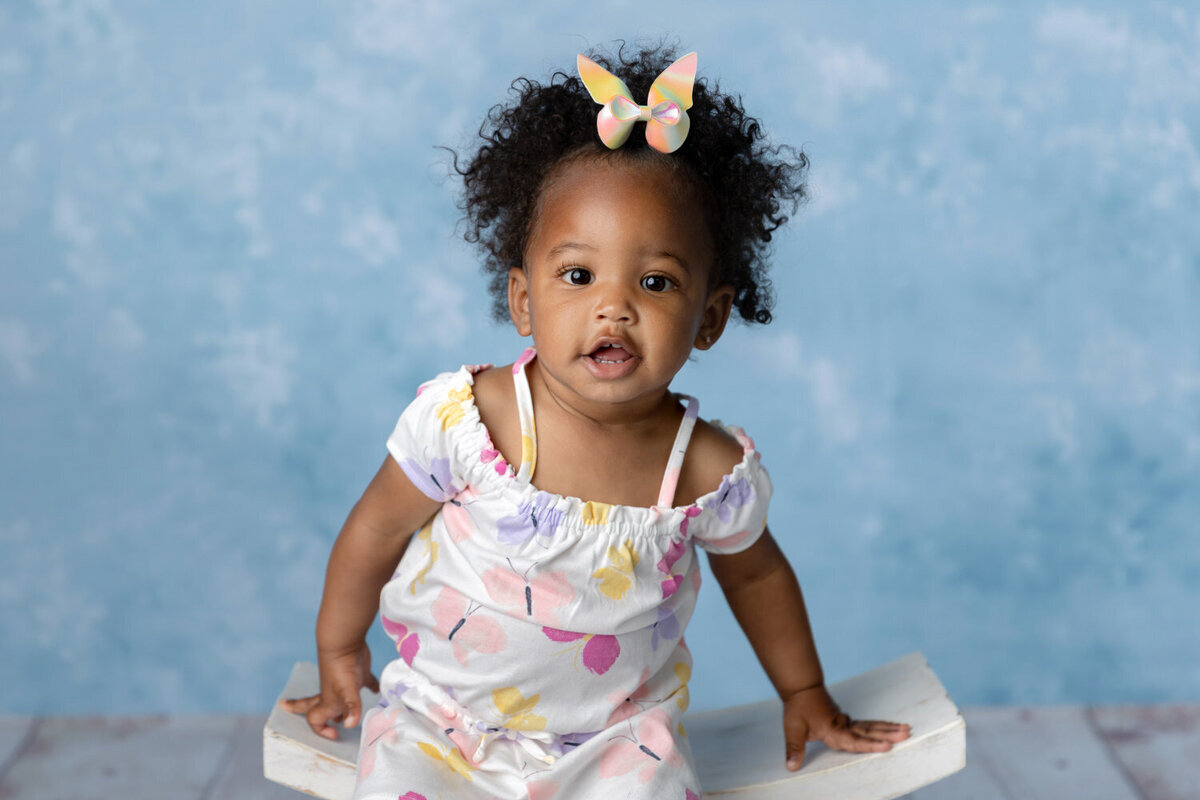 Baby girl in a butterfly dress poses for a closeup photo on a blue background