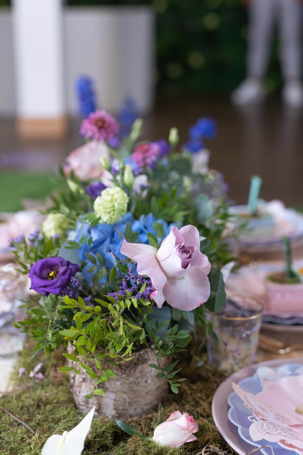 Purple and blue flower arrangements on a moss runner table setting