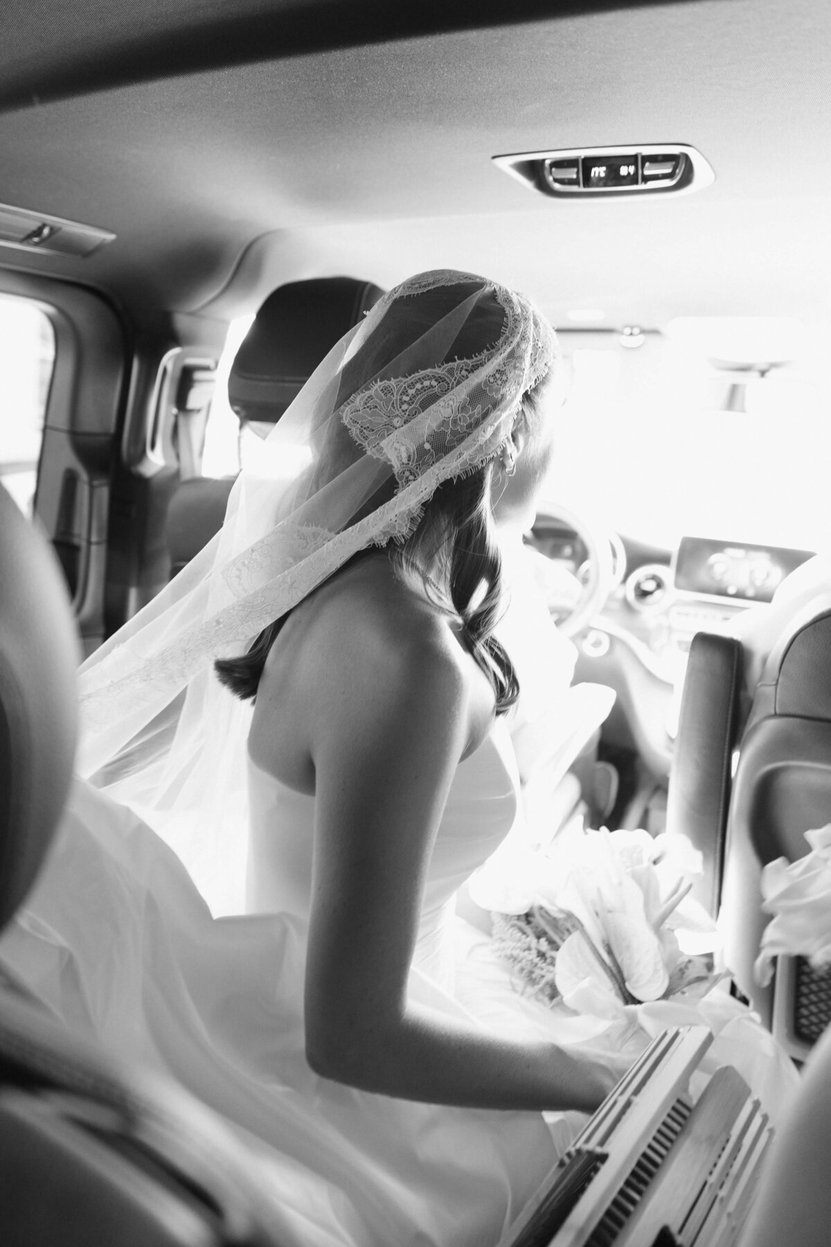 Bride sitting in car in her wedding dress, captured through the window