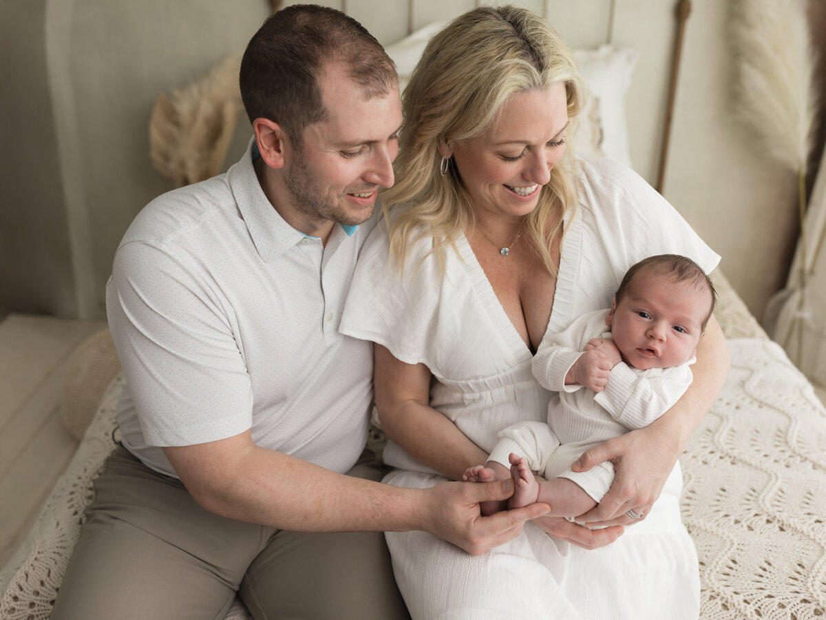 mom and dad holding newborn baby boy in white onesie for studio lifestyle session 
