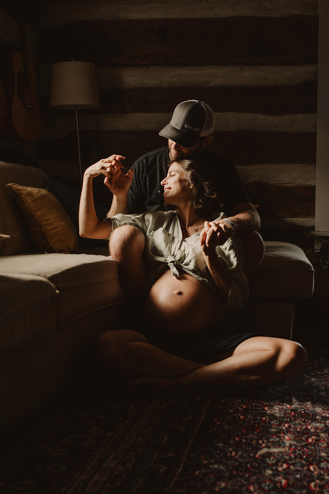 A pregnant person sitting on the floor as their partner sits behind them 