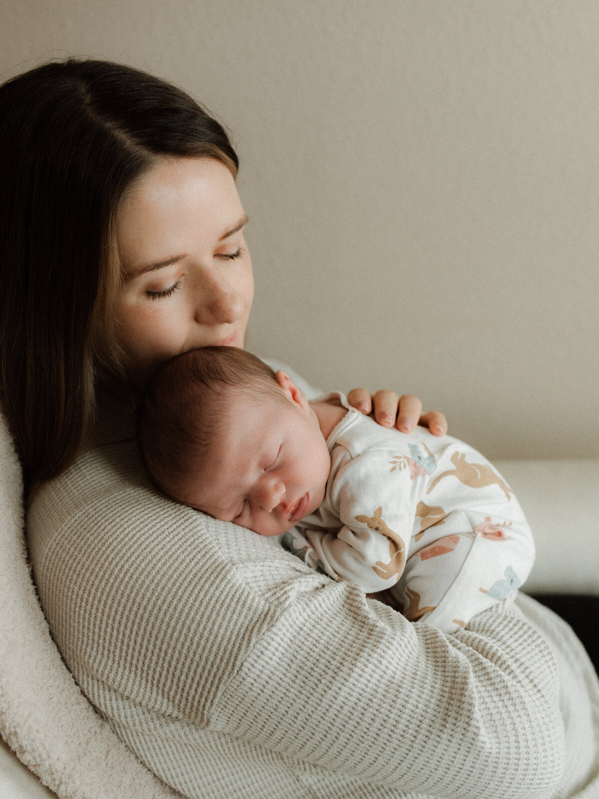 Mother cradles her peacefully sleeping baby on her shoulder during a natural light lifestyle session at home.