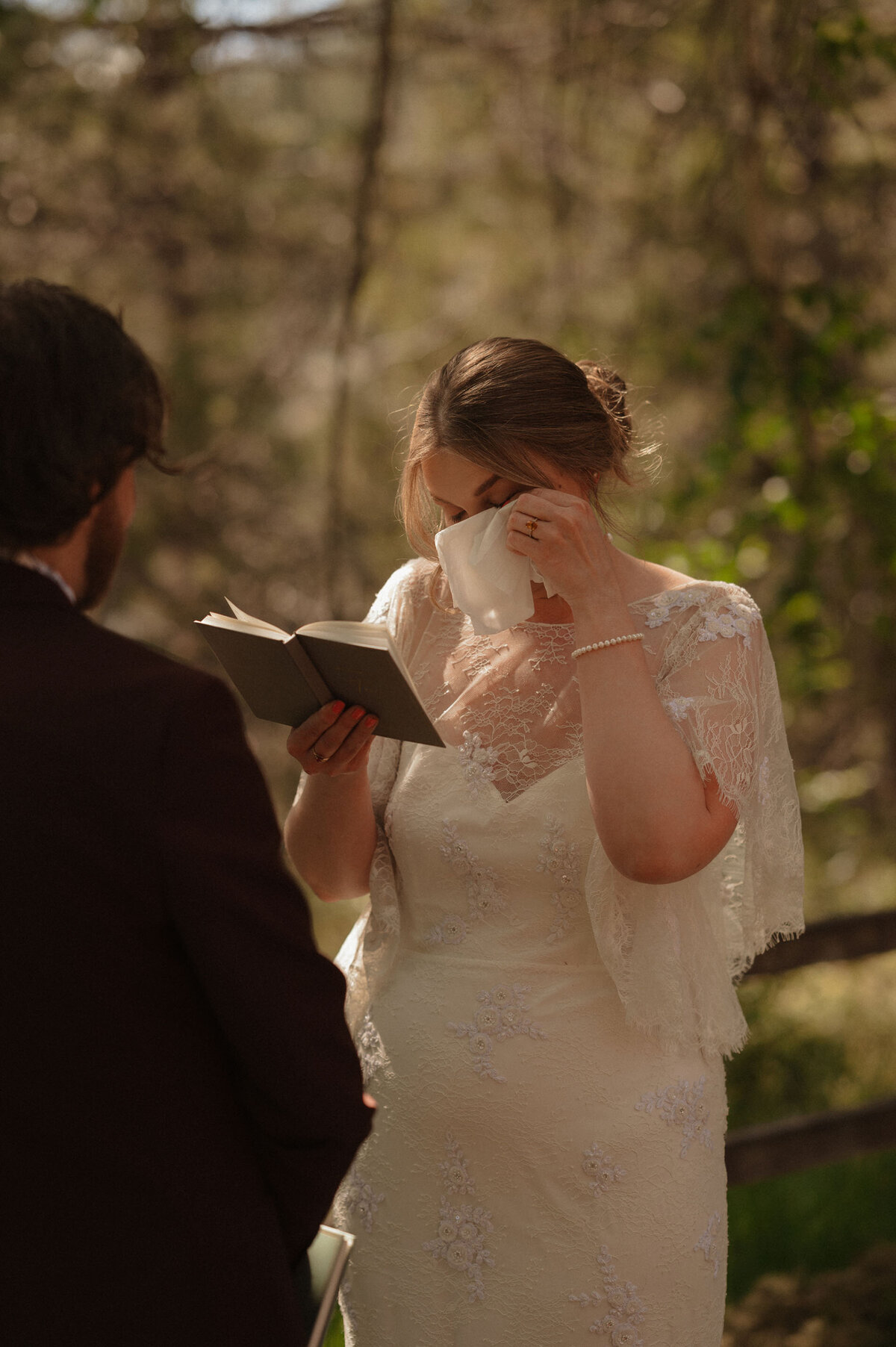 bride wipes away tears with a tissue as she reads her vows to the groom on a summer day in Bend, OR