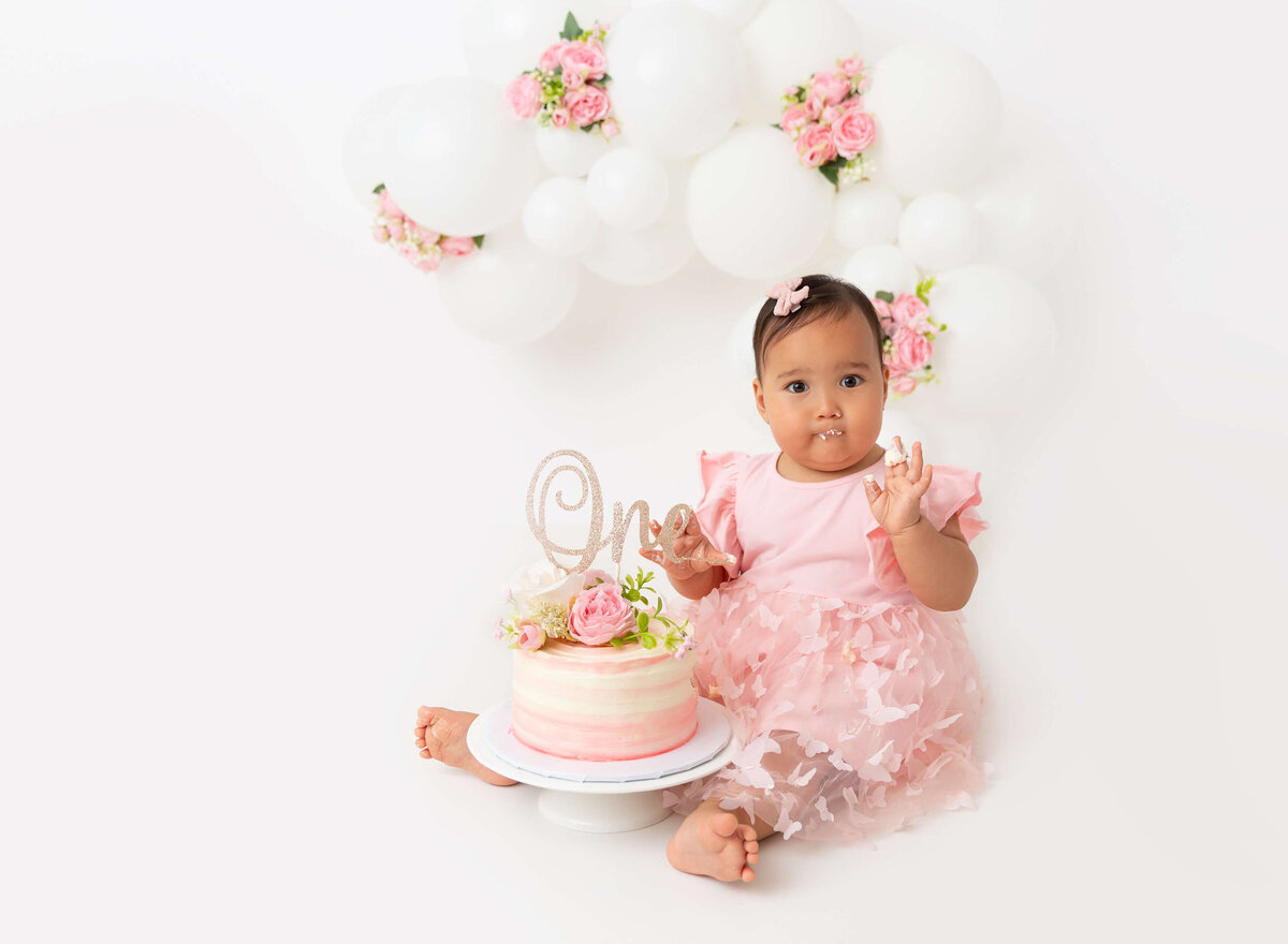 Baby girl pink and white flower cake smash with a balloon garland