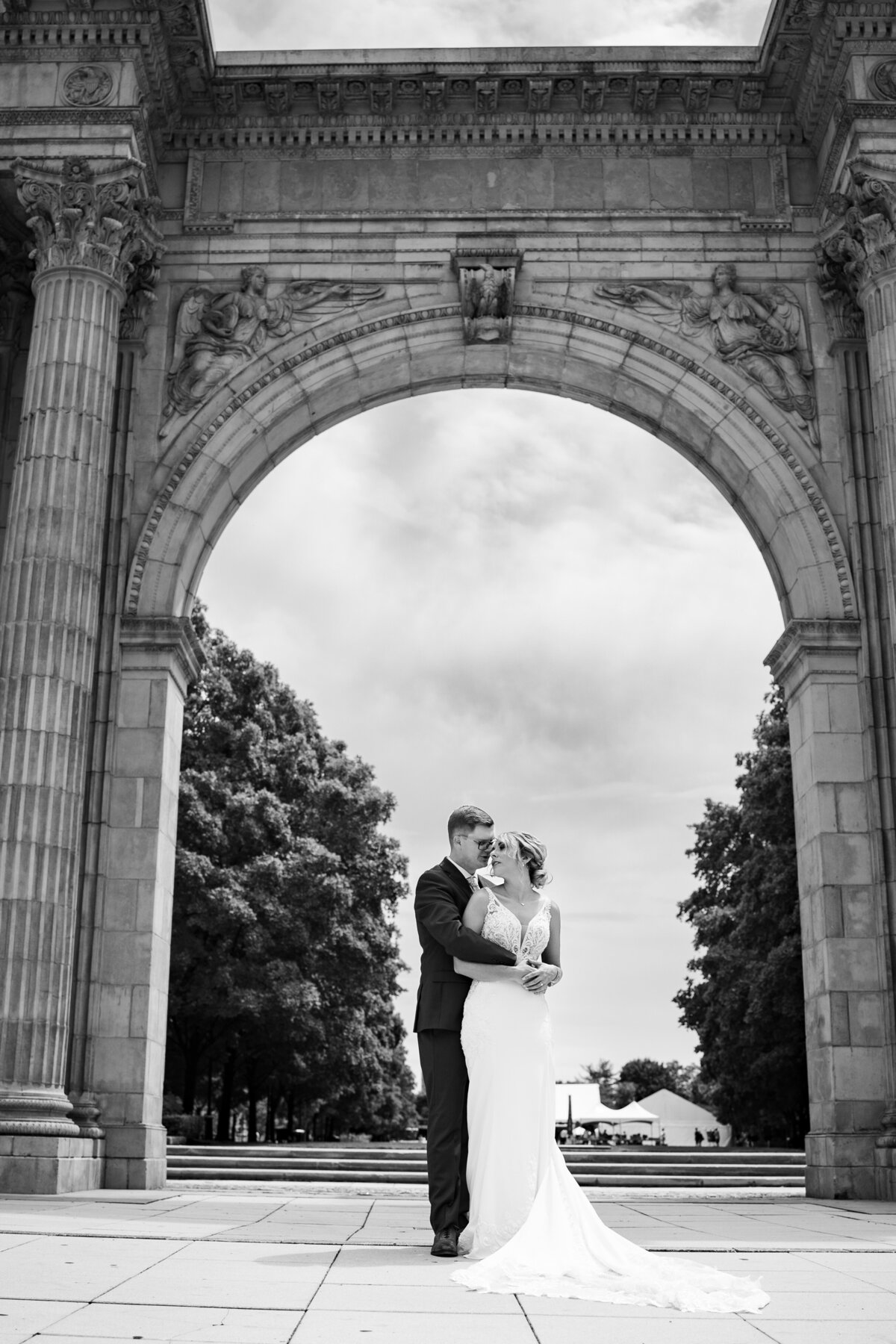 Groom wraps his arms around his bride and they touch heads under a large, detailed arch at the Arena District in Columbus, Ohio.