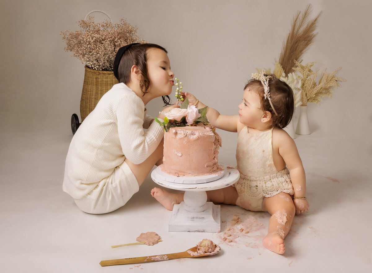 Little sister feeds her big brother cake at her first birthday cake smash photoshoot in brooklyn, ny. Captured by Chaya Bornstein brooklyn milestone photographer