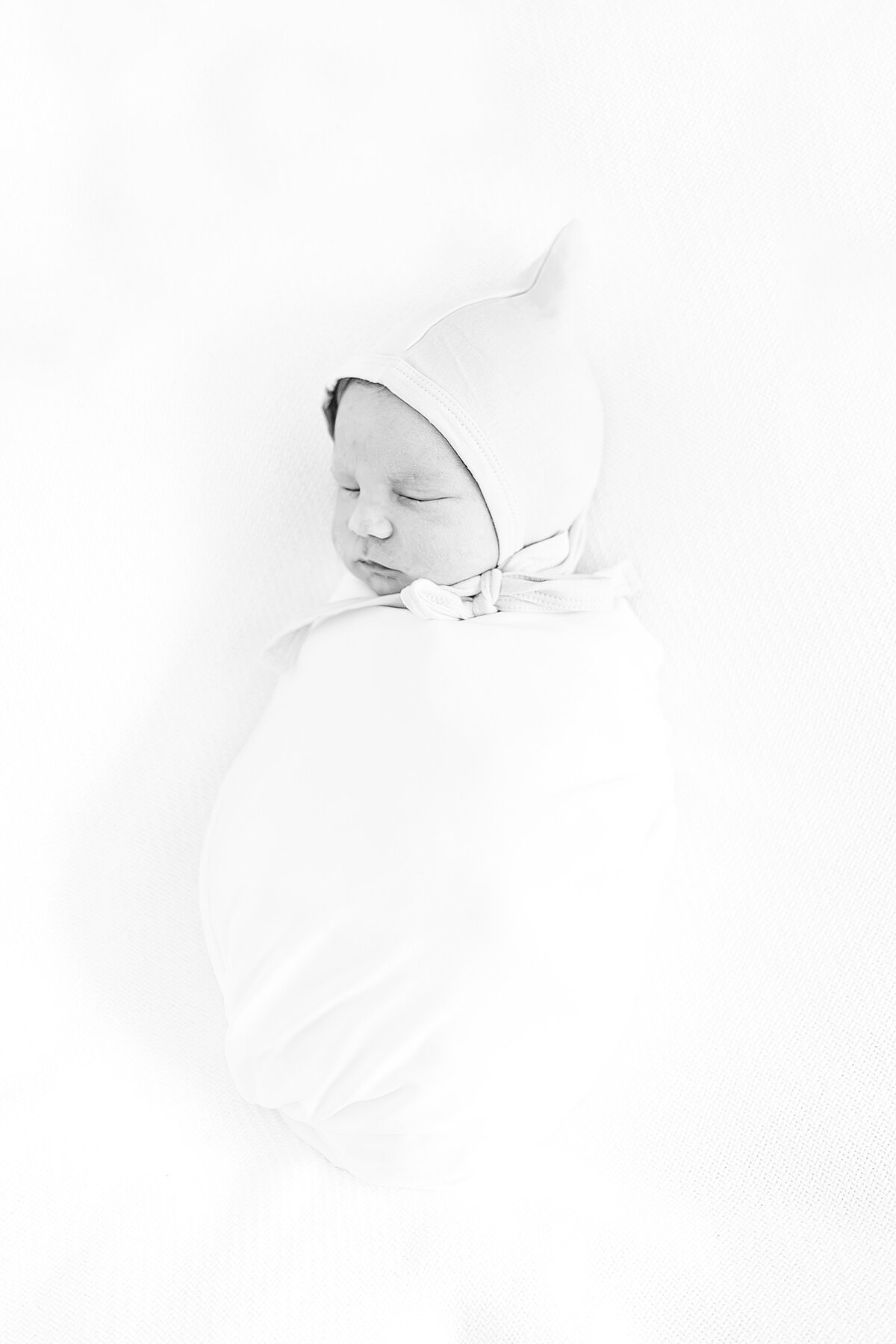 black and white picture of newborn baby boy swaddled with gnome cap on sleeping with eyes closed
