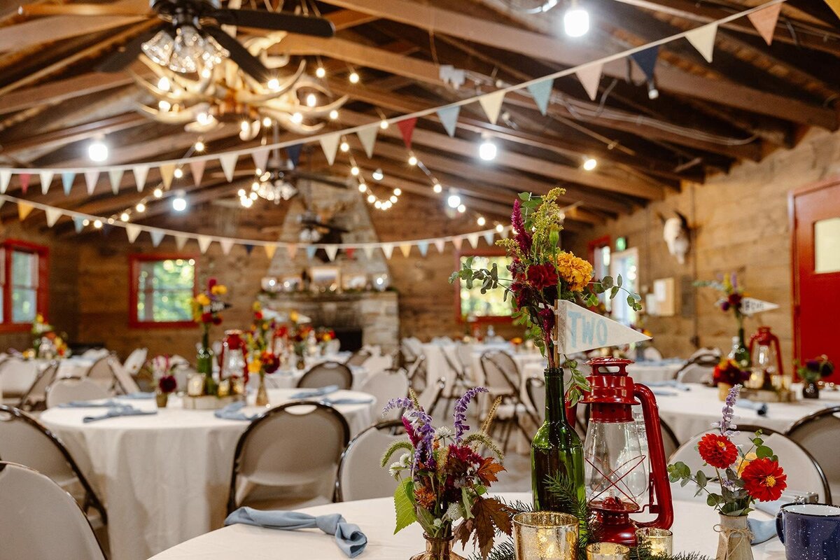 Table scapes at a summer camp wedding featuring red lanterns, hanging pennant flags