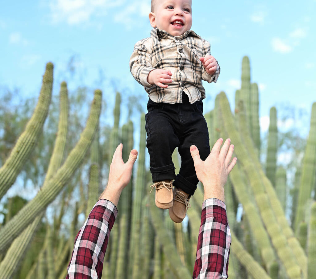 A baby smiling while being thrown in the air by their parents.