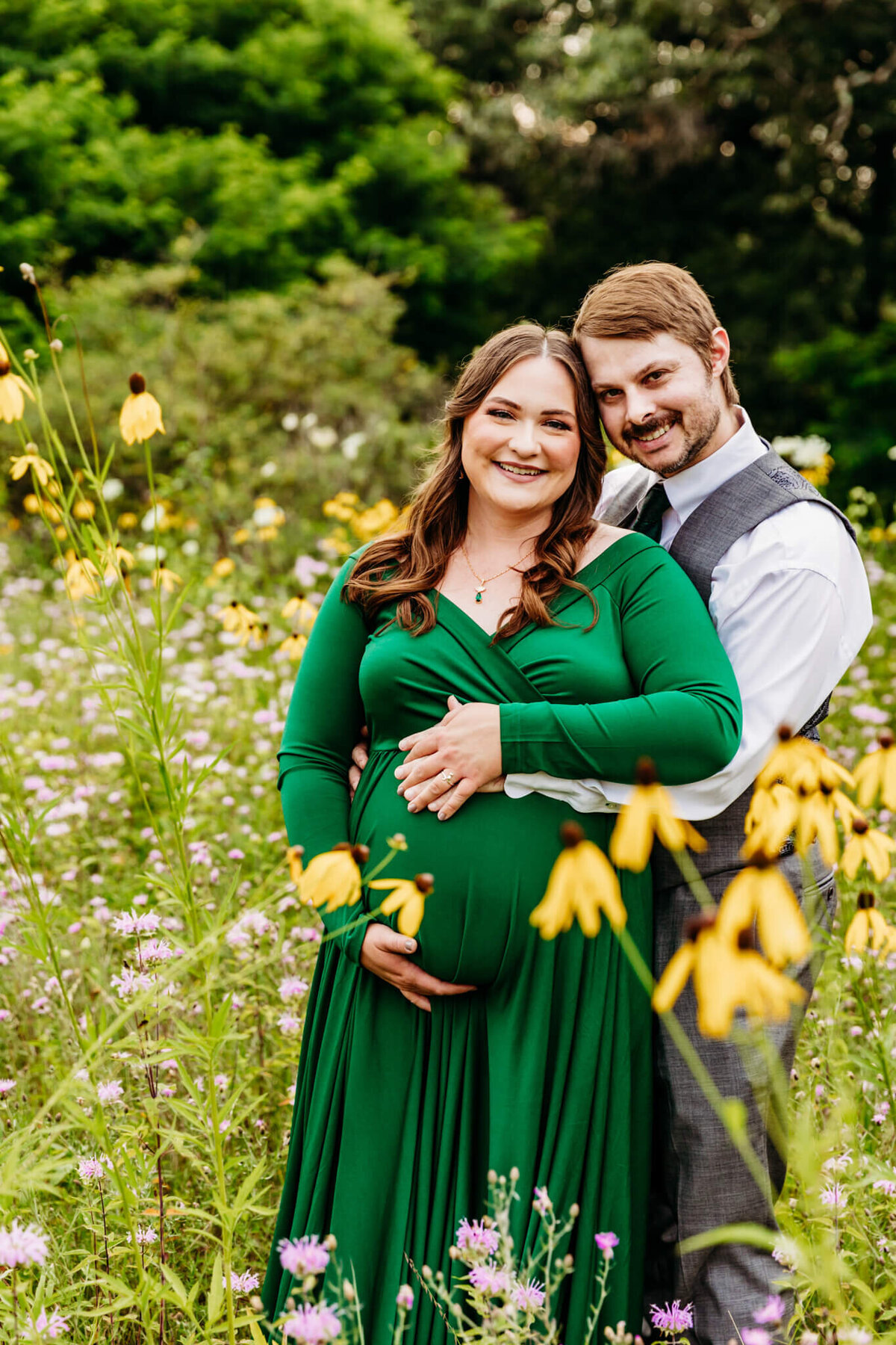 gorgeous parents embracing their baby bump and smiling as they stand in a wildflower field near Green Bay WI