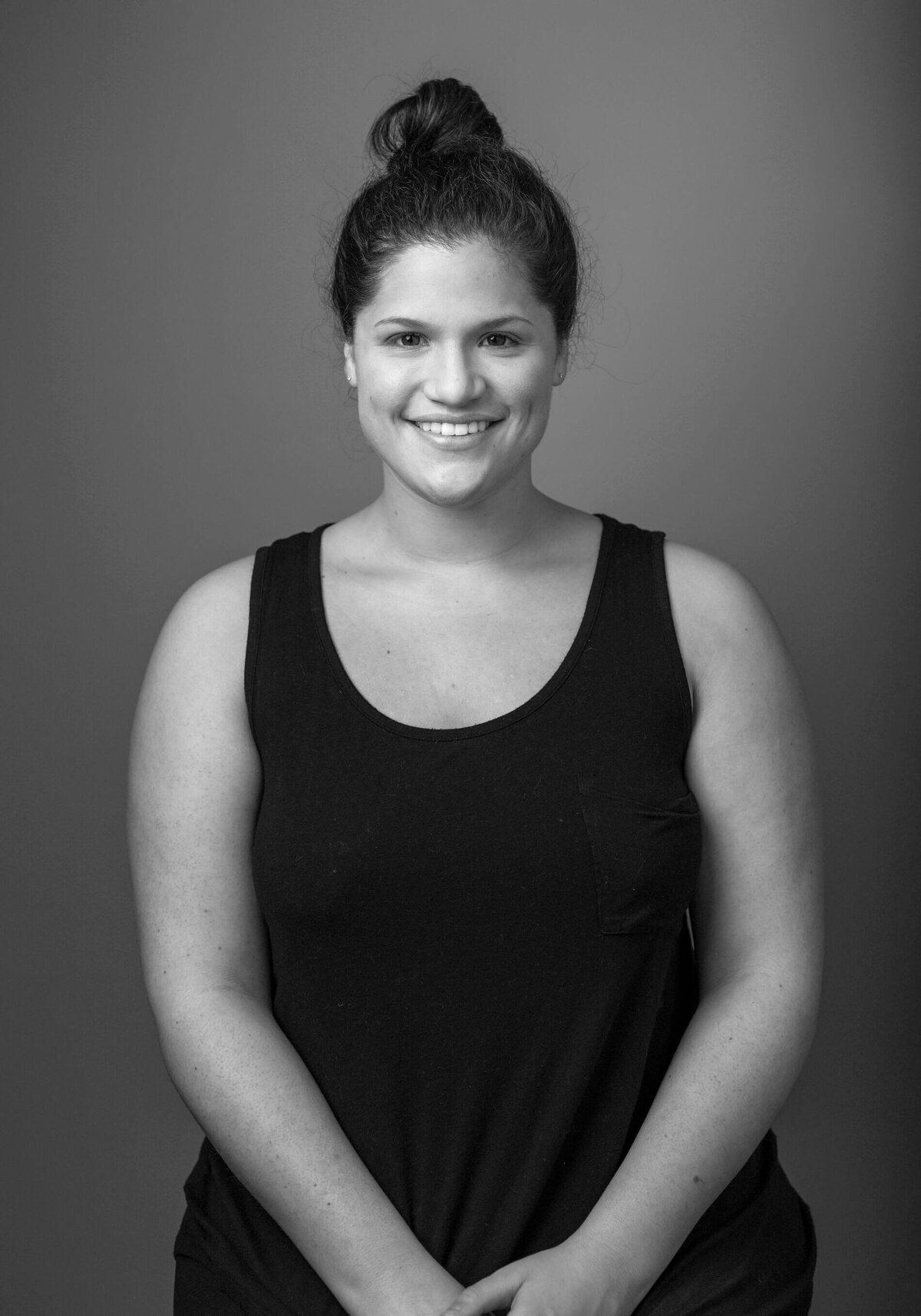 Studio before shot of a woman in a black tank top, smiling with her hair in a bun.