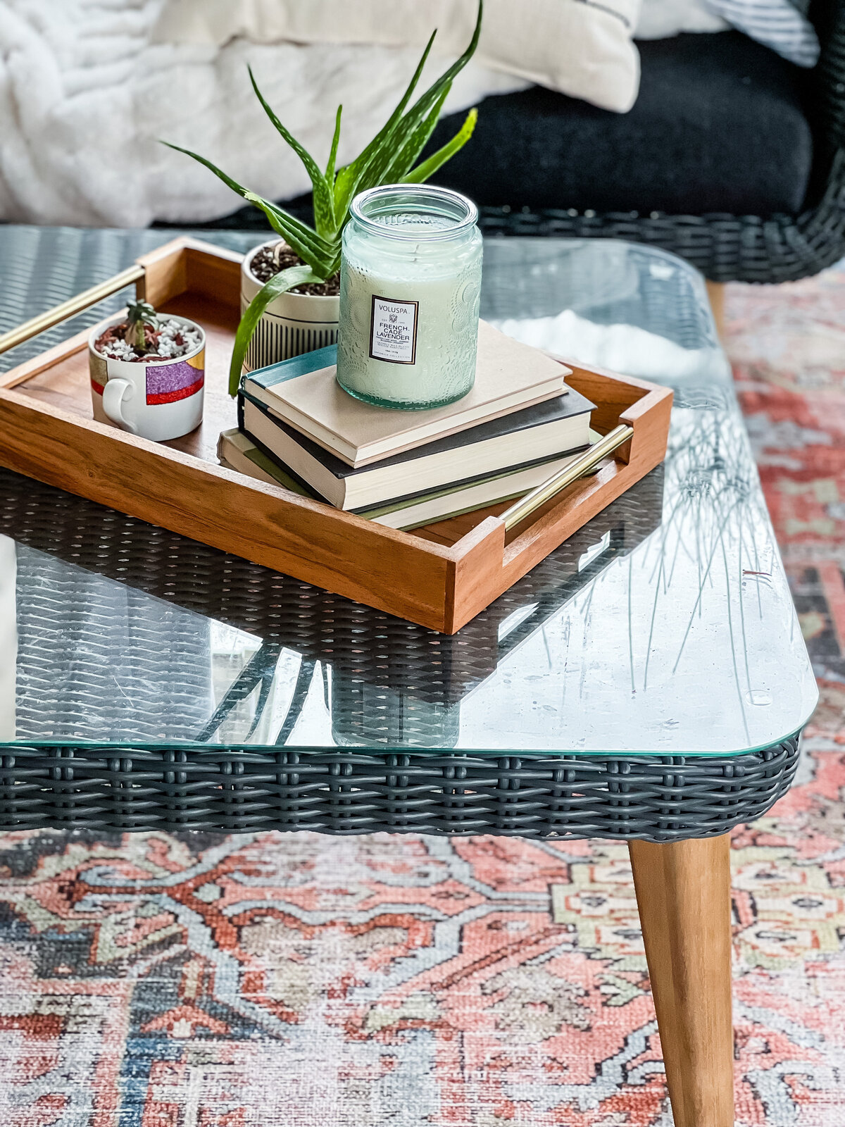 A glass top coffee table holds a wood tray with books and a candle