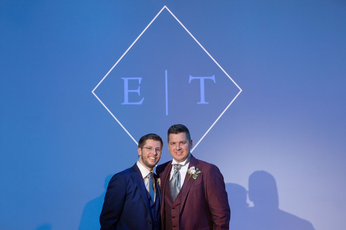 Two men in suits pose in front of a blue background 
