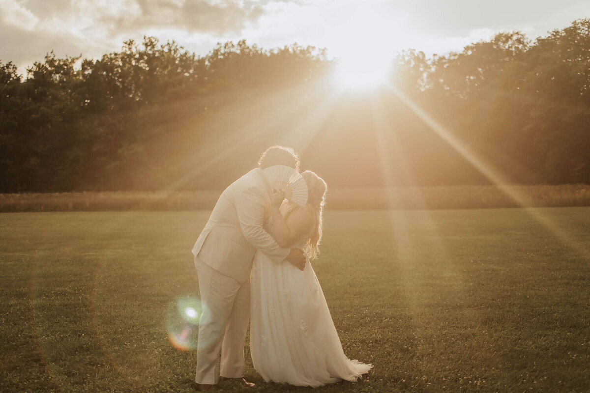 Bride and groom sharing a kiss at sunset in a wide, open field