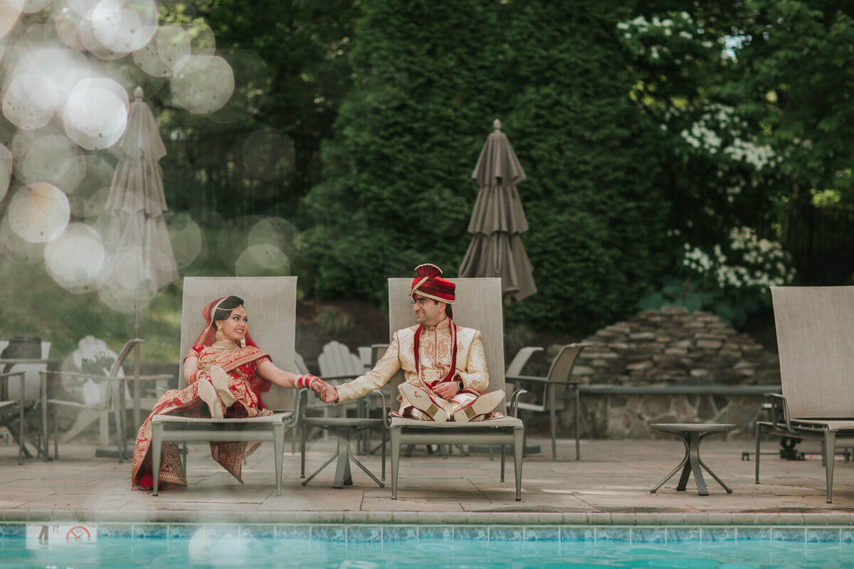  bride and groom in traditional attire relax poolside, holding hands and sharing a lighthearted moment. Wedding in King Of Prussia