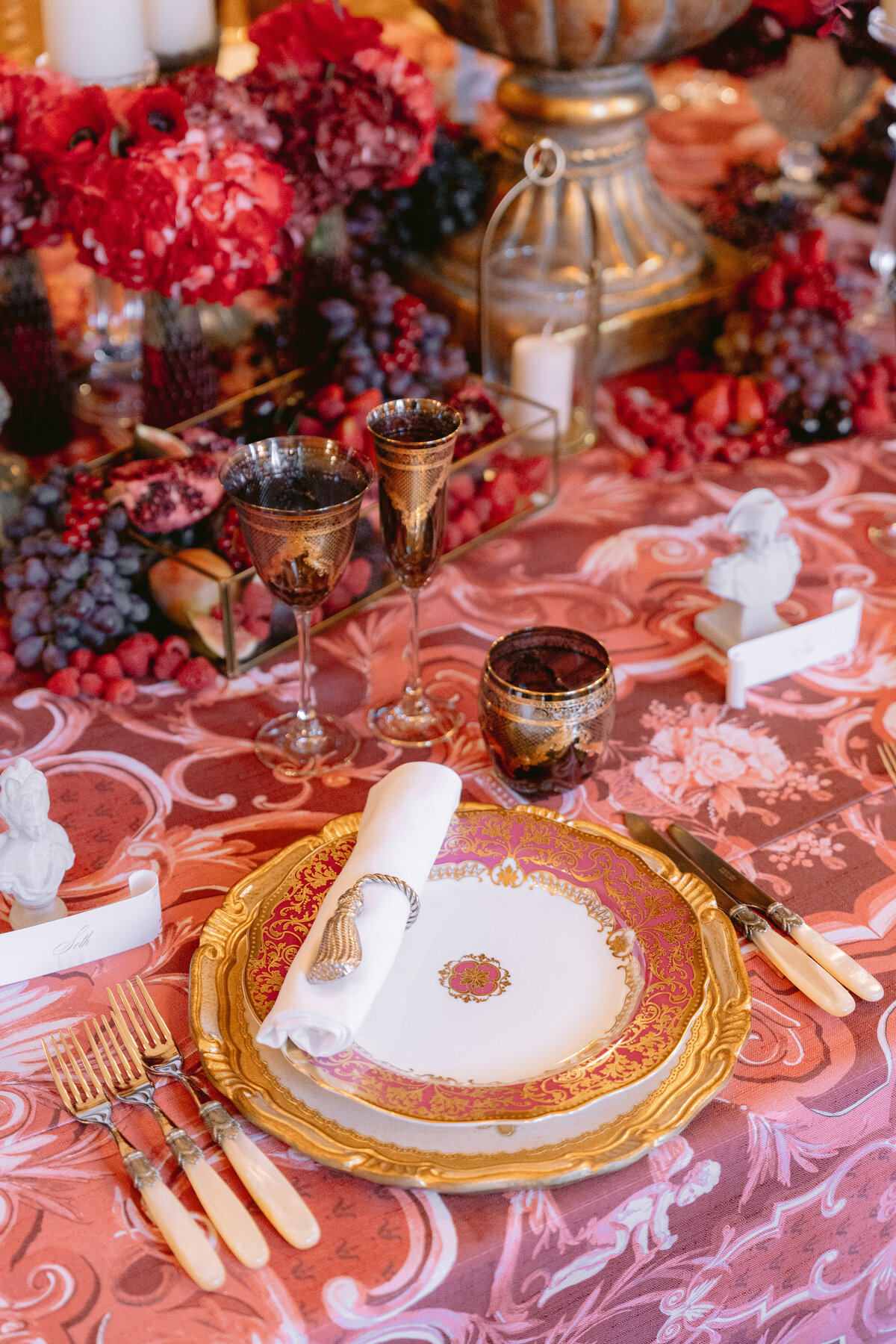 The stunning photo was captured by the talented photographer Matteo Coltro at the exquisite Shangri La Hotel & Ritz Paris Hotel in Paris, France. The videography was expertly done by Zen Film Works. The lavishly set dining table showcases an ornate gold and pink plate with carefully arranged cutlery, a beautifully folded napkin secured by a chic napkin ring, as well as elegant glassware. The table is further enhanced by a richly patterned tablecloth that complements the setting, while decorative items and vibrant floral arrangements add a touch of luxury and sophistication to the scene.