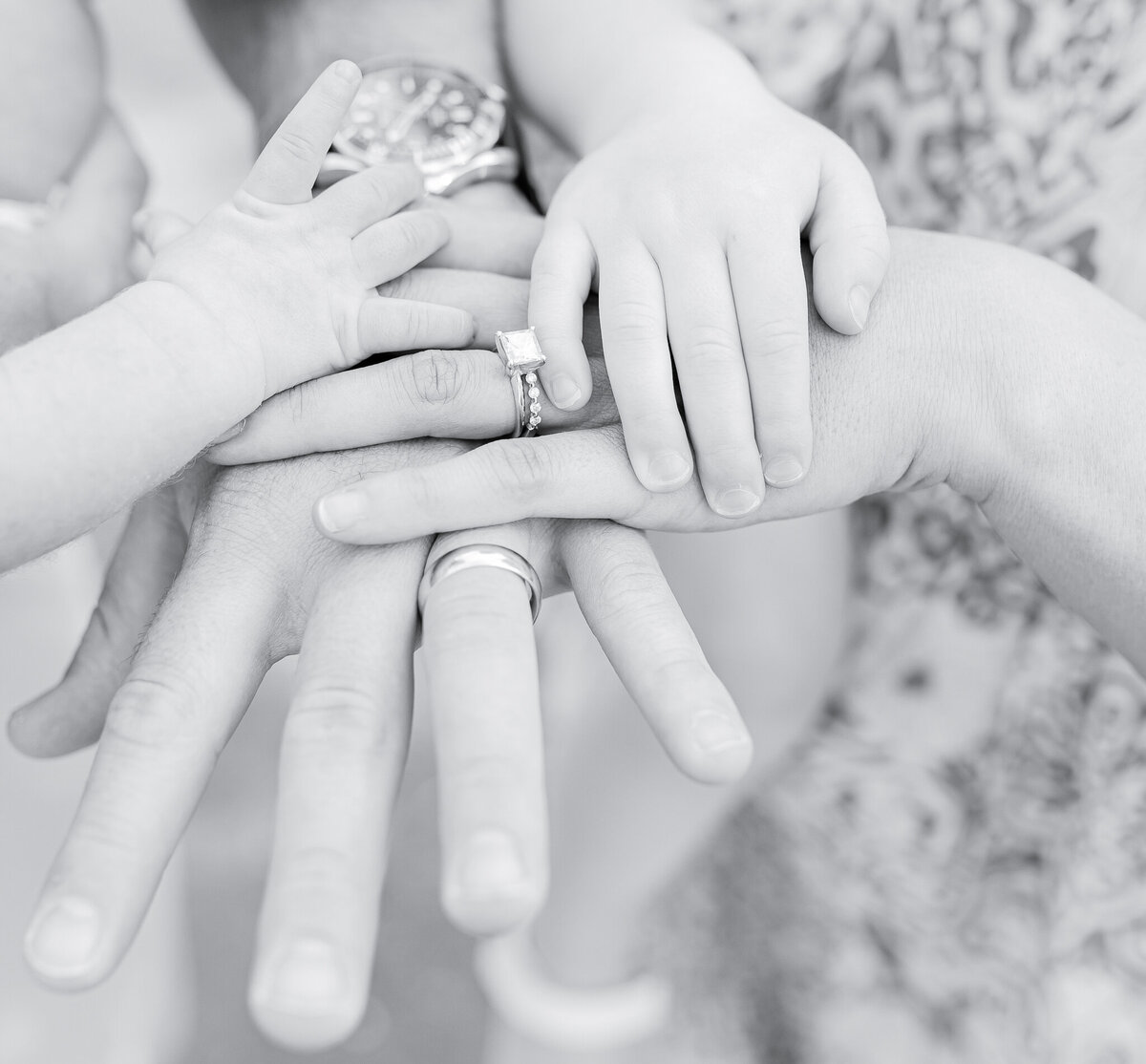 Close-up of family hands stacked together – newborn photography in Birmingham. A newborn's tiny hand rests gently on top of their parents' and sibling's hands, capturing the warmth and connection of family life.