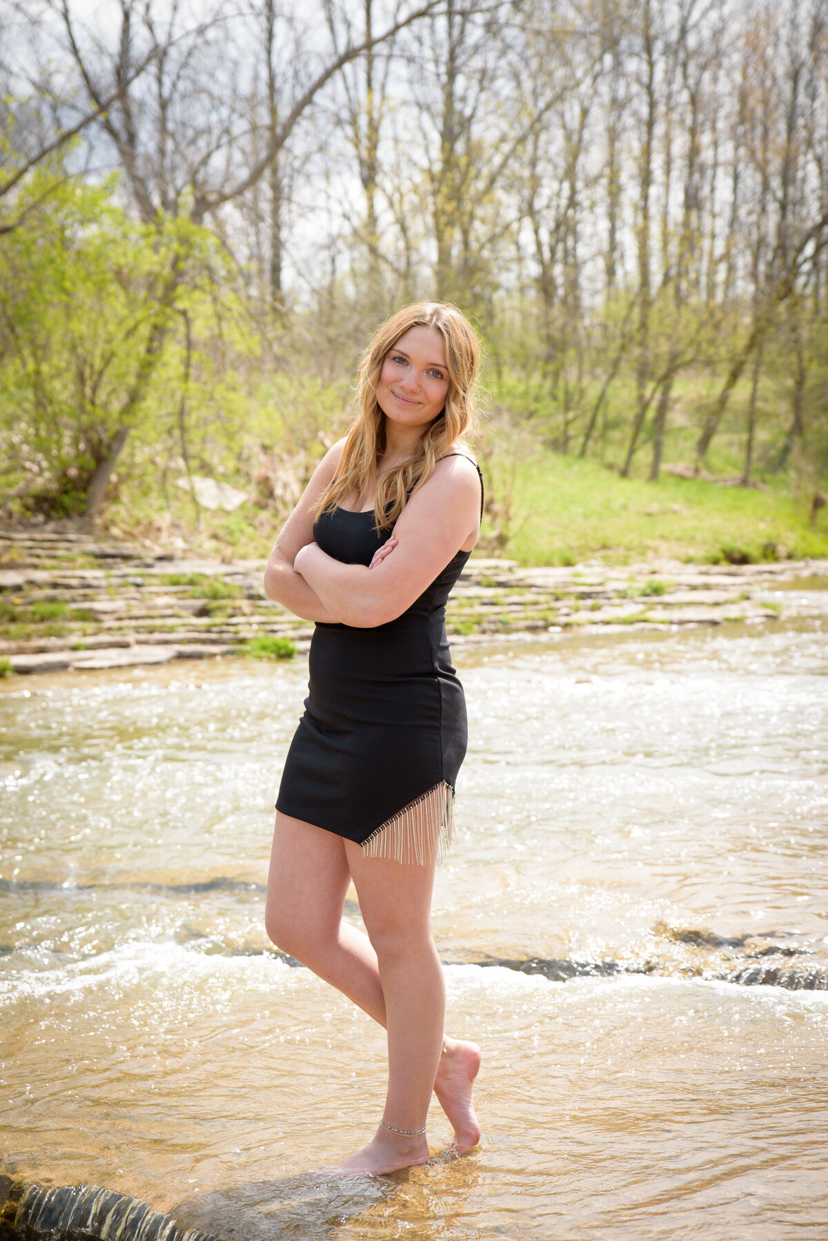 high school senior girl standing bare feet in creek wearing a short black dress at Fonferek Glen in Green Bay, Wisconsin