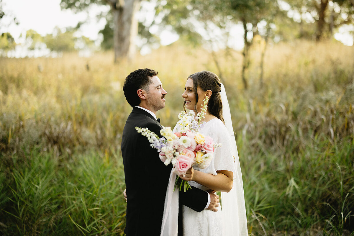 Vibrant Red rose petals floating in the air over bride & groom with bride holding her bespoke wedding flowers