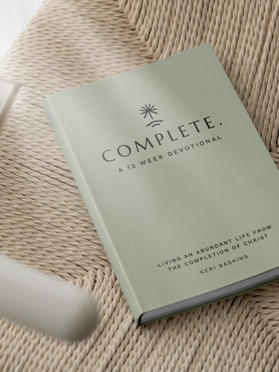 Hardcover print version of the “Complete” devotional by Keri Baskins featuring the MPR Ministries logo and soft sage cover, resting on a woven chair.