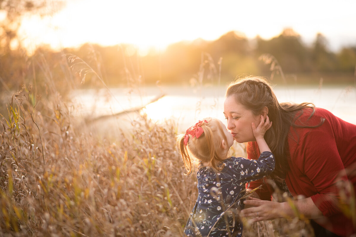 Mom and daughter kissing in the sunlight in a field in Richmond.