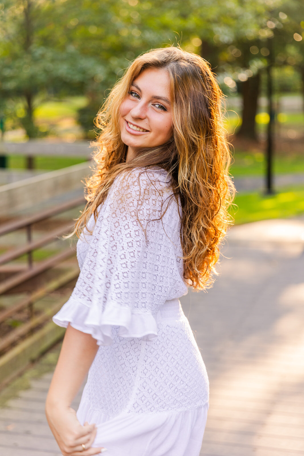 senior gilrs wearing a white dress looking at the camera over her shoulder on an Atlanta park at golden hour