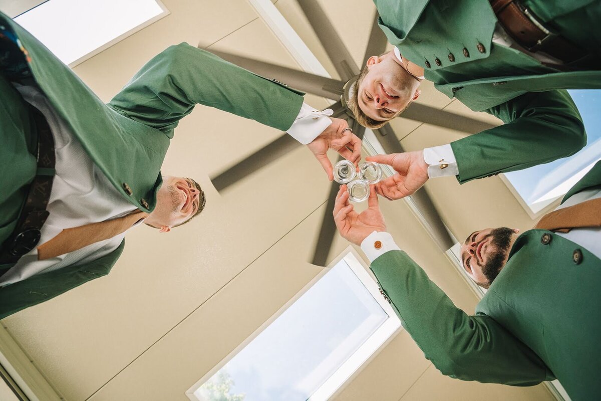 Groom and groomsmen share a drink before the wedding ceremony in green tuxedos.