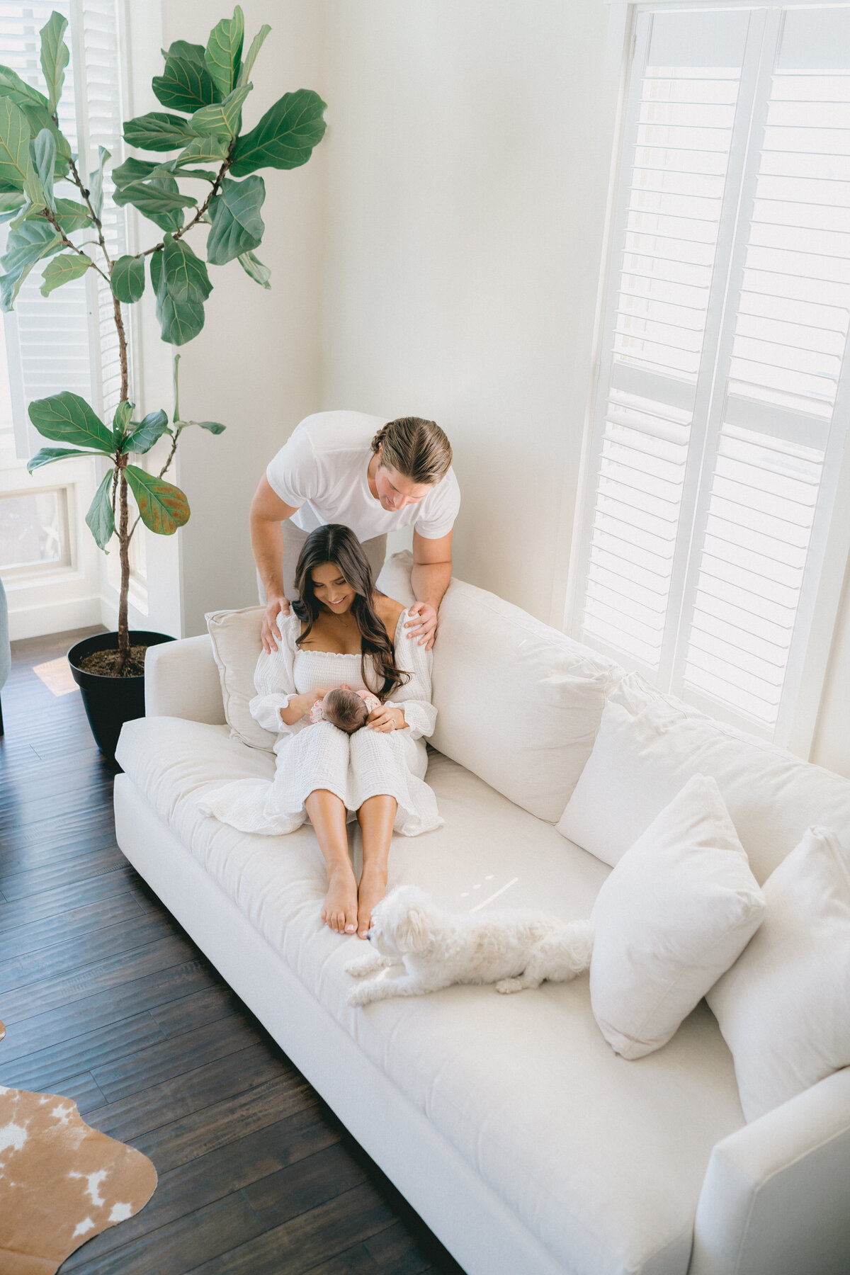 In-home newborn photography session featuring parents and their baby near a window, by Salt Lake City Family Photographer.