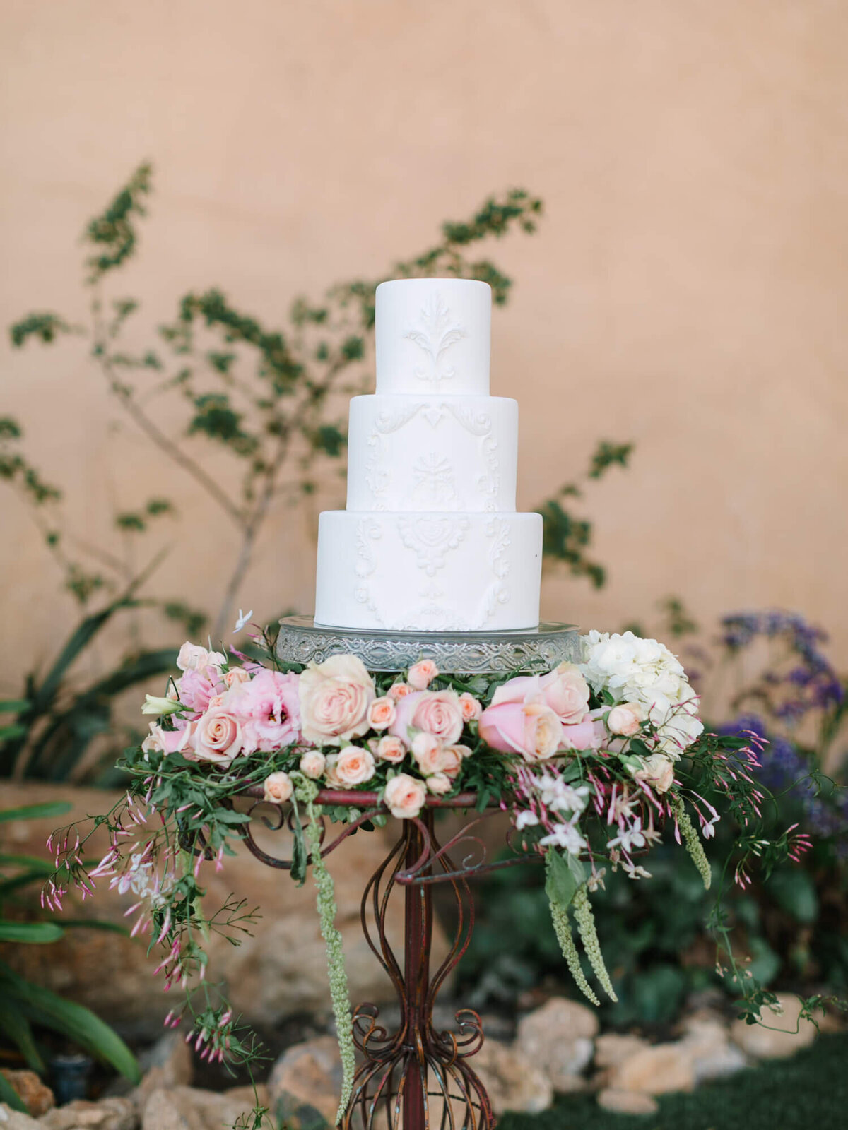 Three-tiered white wedding cake with intricate detailing, placed on a decorative stand.