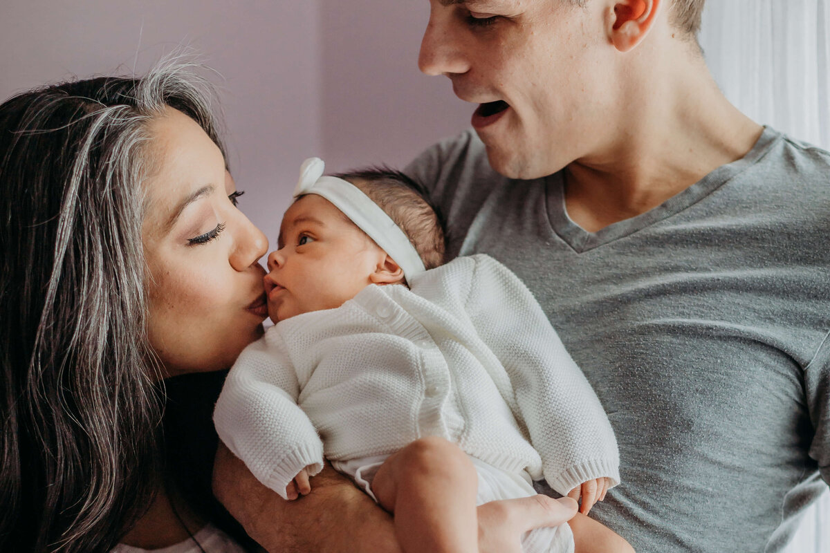 new parents kissing newborn in natural light by luci levon photography