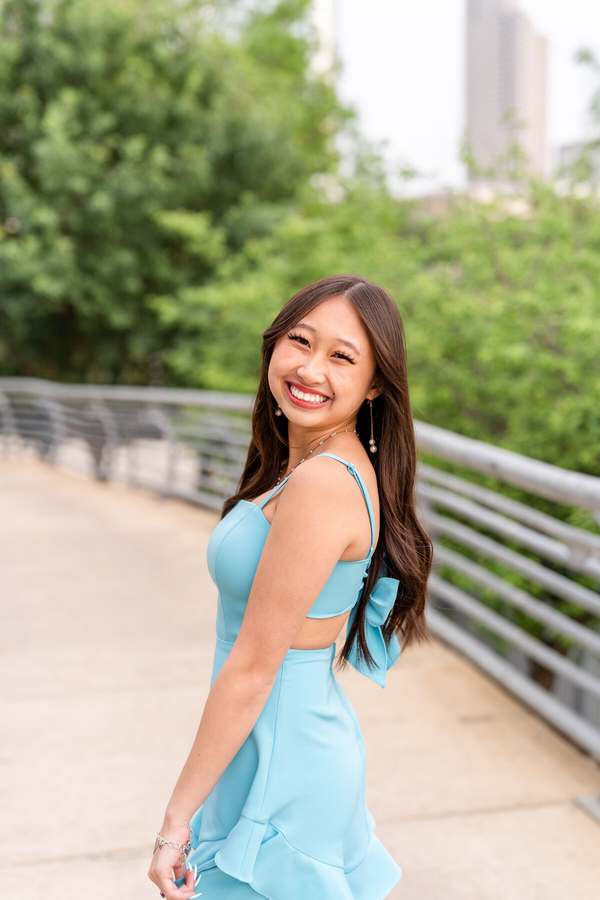 Houston high school senior girl laughing over shoulder while wearing baby blue dress and a bow with Downtown Houston in the background