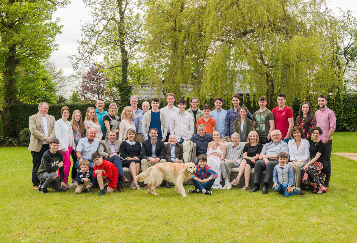 Portrait of a large extended family with golden retriever dog in a garden surrounded by weeping willow trees