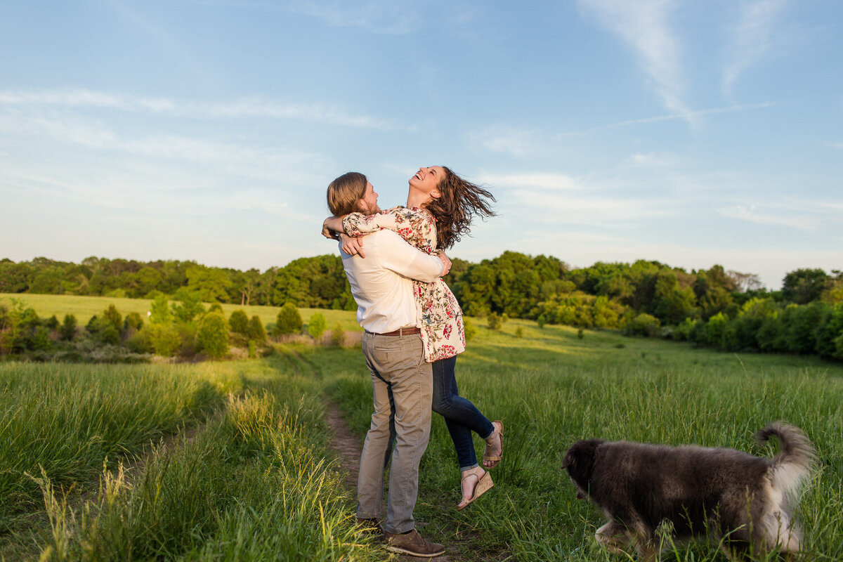 engagement photo of a joyful couple in a field with their dog
