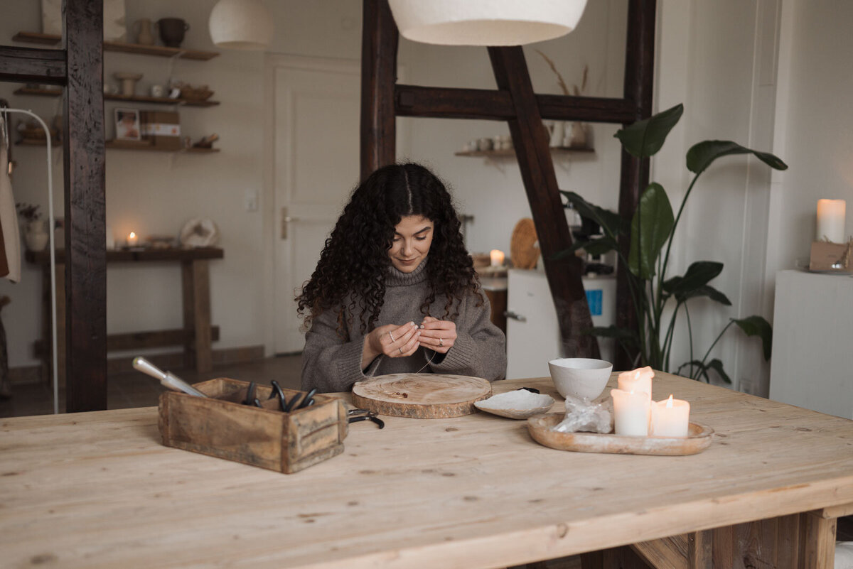 eine Frau sitzt in ihrem Atelier und kreiert ihren eigenen Schmuck
