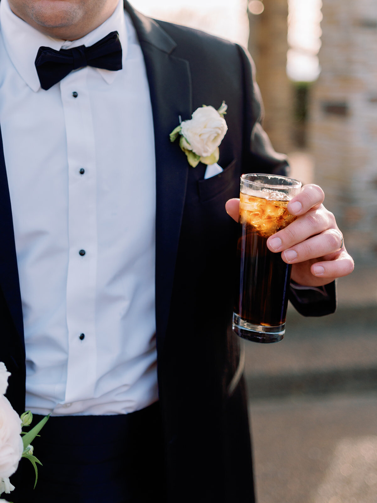 Close-up of the groom in a black tuxedo holding a cocktail glass during the wedding celebration at Burritt on the Mountain in Huntsville, Alabama, photographed by Perry Hancock.