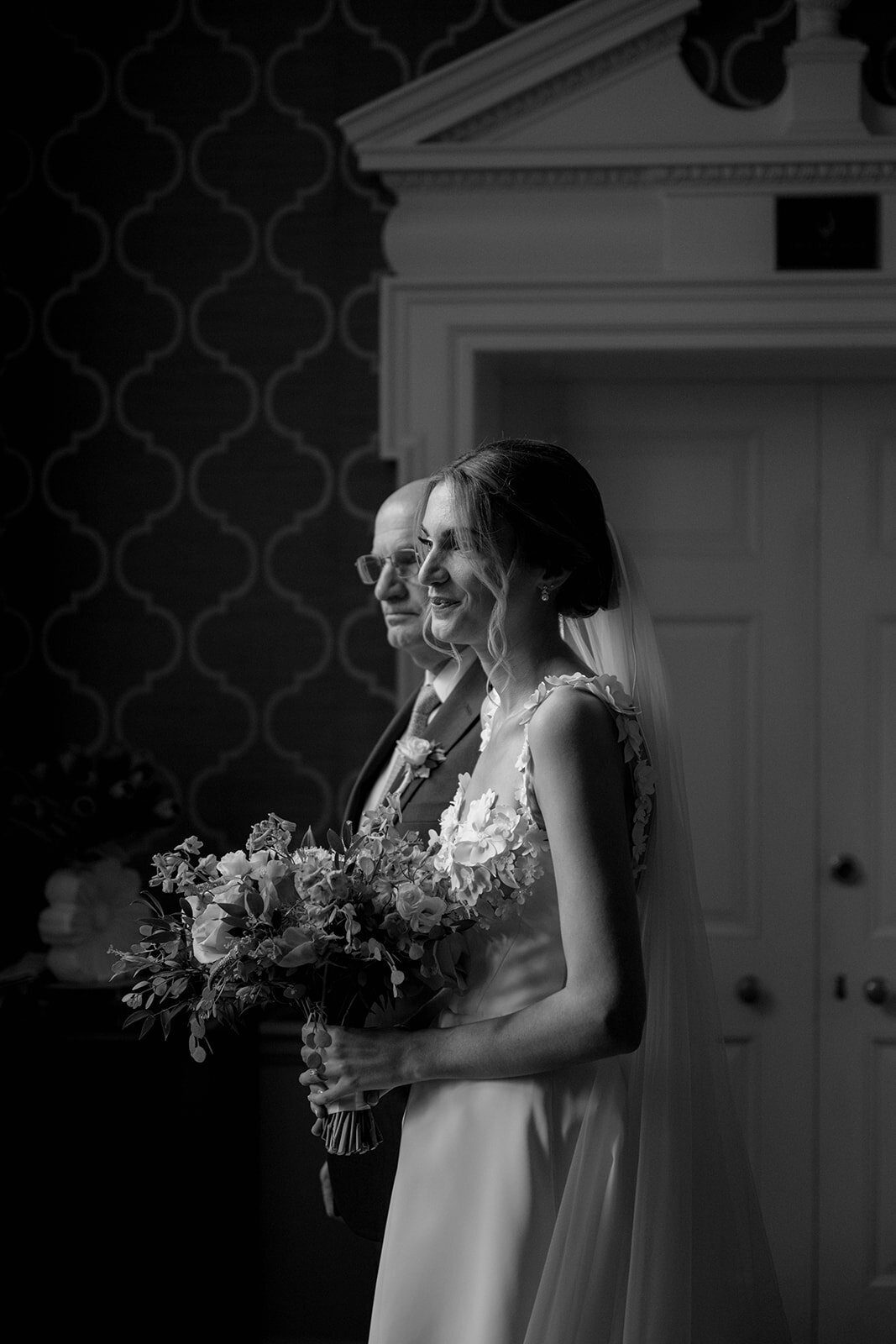 Black and white photo of a bride standing with a smile while holding her bouquet